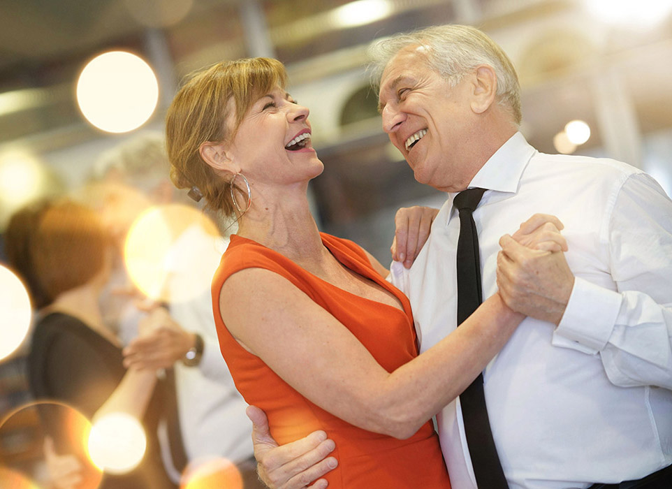 Eldre par danser og ler sammen.