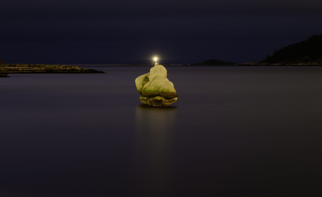 Blikkstille hav med fyrlykt i bakgrunnen